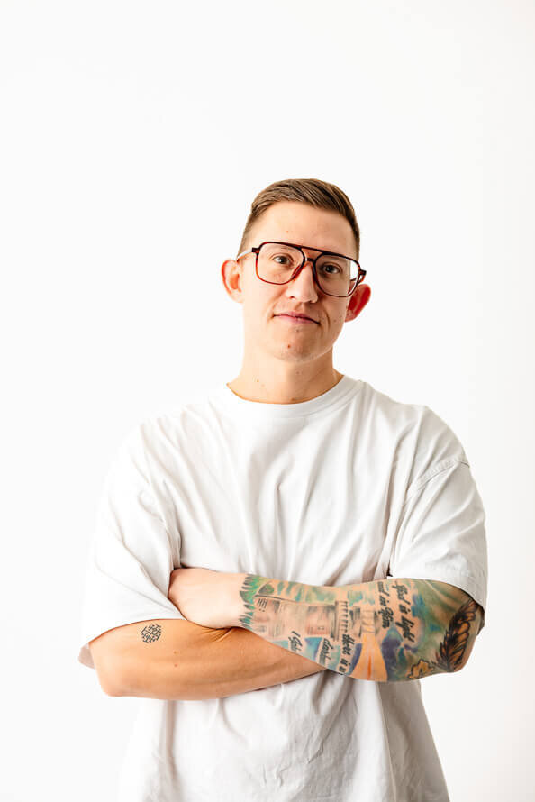 Man in white shirt with tattoos folds arms.