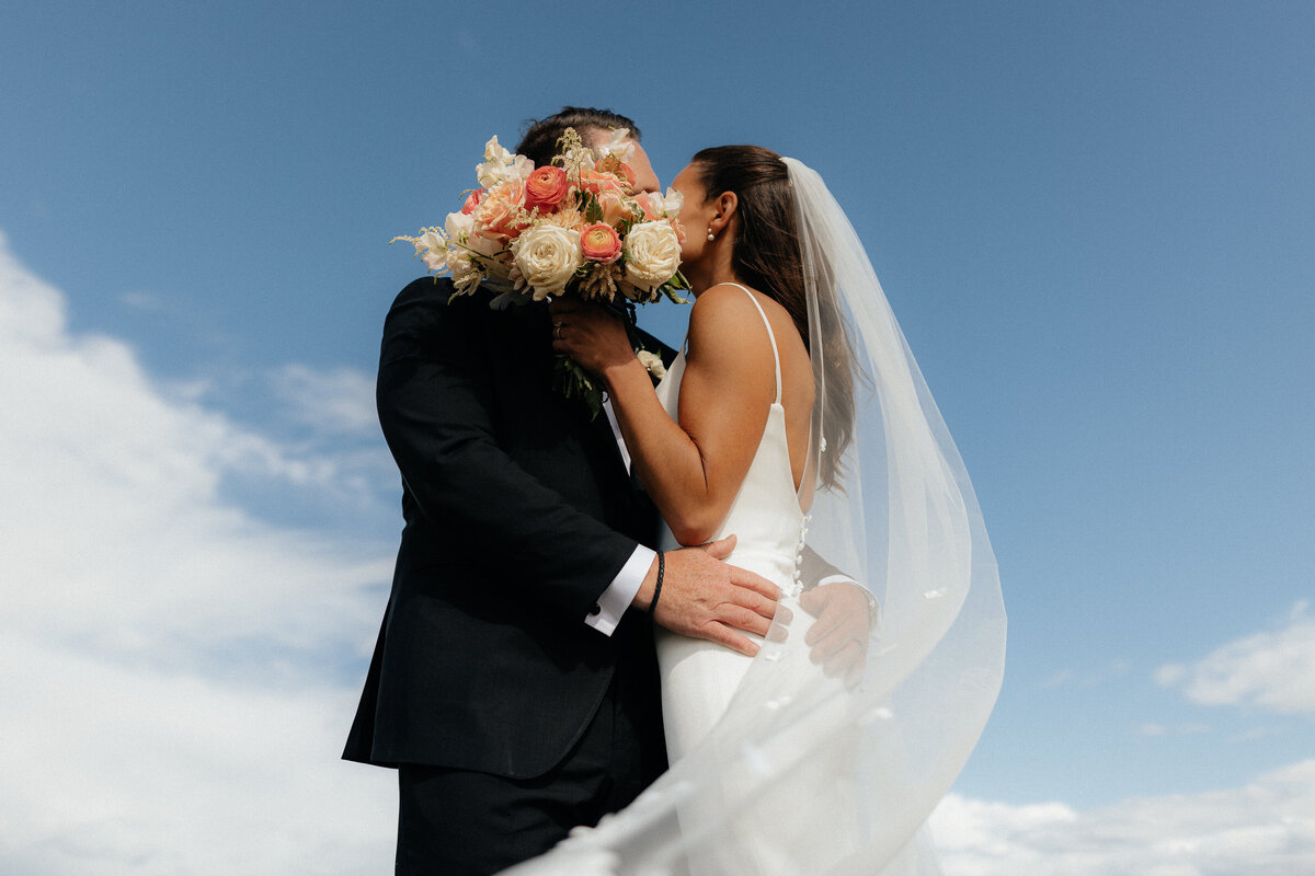 couple kissing behind calgary wedding bouquet