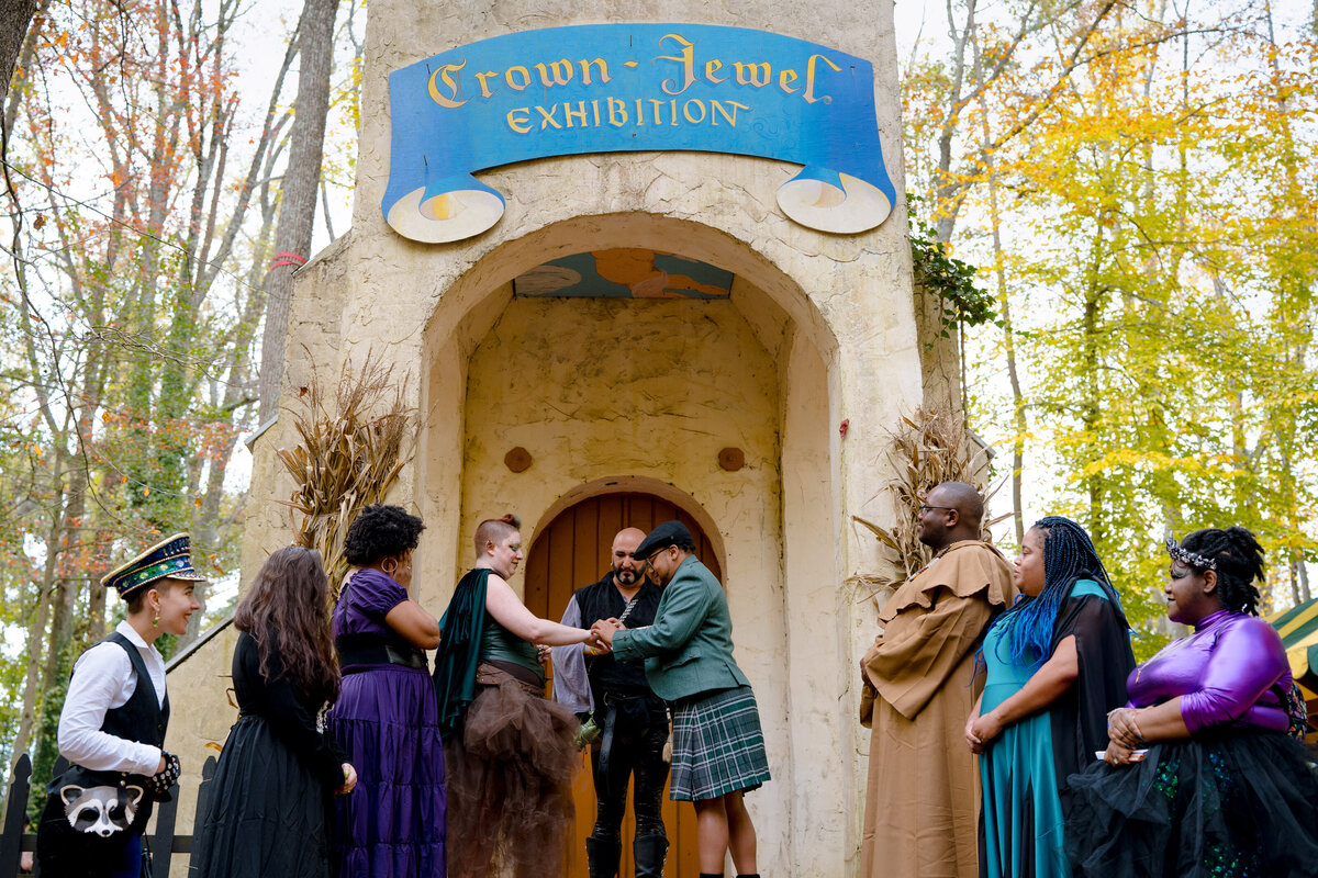 A wedding couple and their wedding parties standing on the stairs to a whimsical building as they exchange rings.