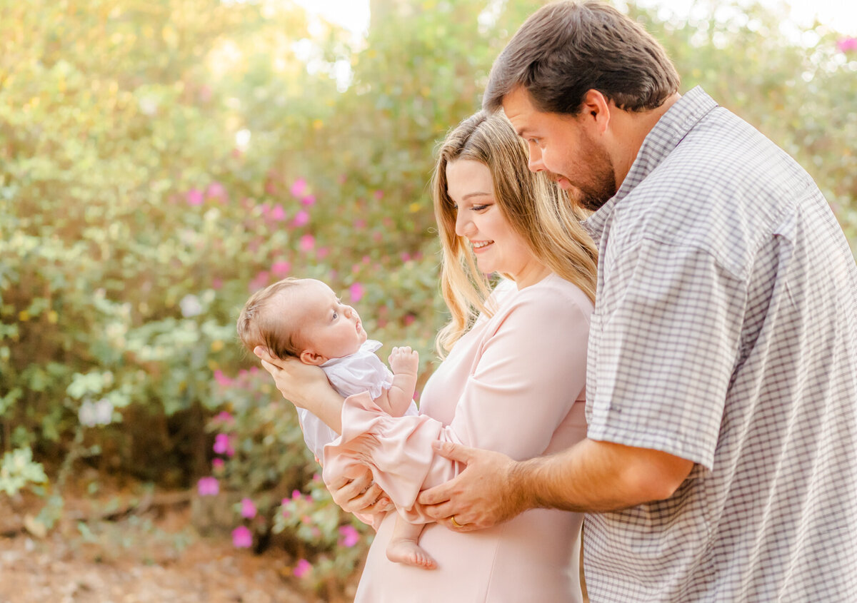 mother holding baby girl while dad talks to her with a colorful background