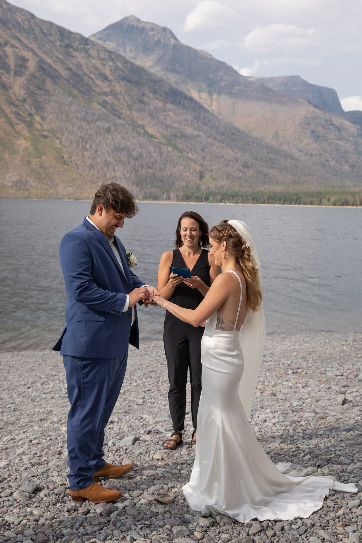 A groom slides the wedding ring on his brides face as the officiant smiles behind them in Glacier National Park.