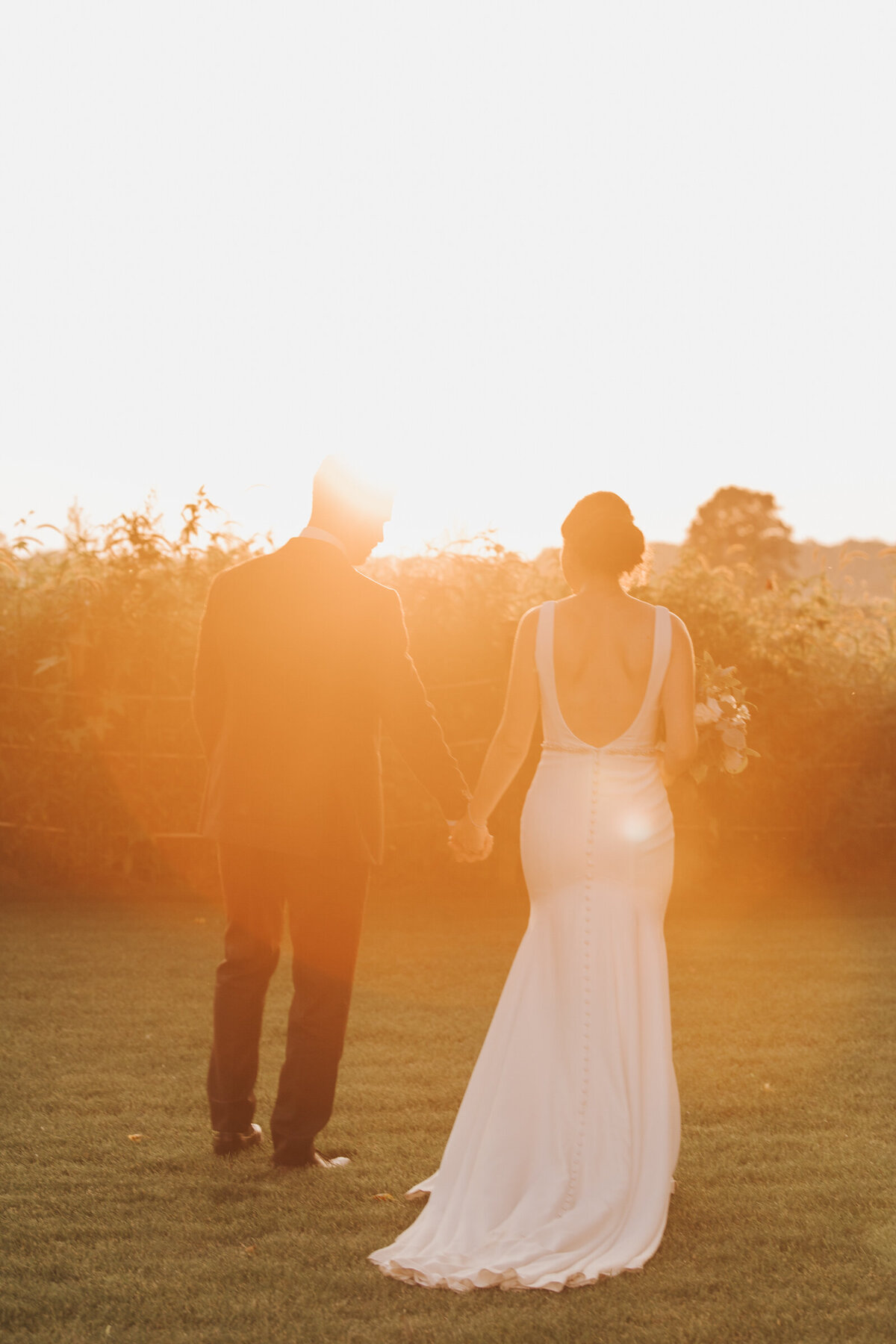 A bride and groom walking hand in hand at sunset on their Summer wedding day