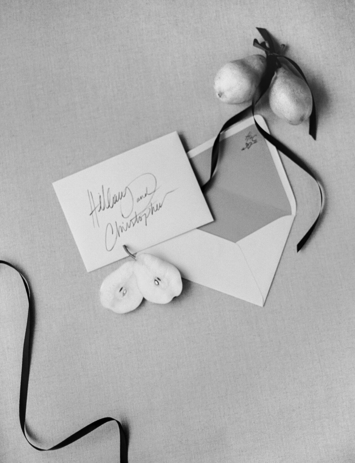 Gestural handwritten wedding stationery rests with sliced pears and black ribbon