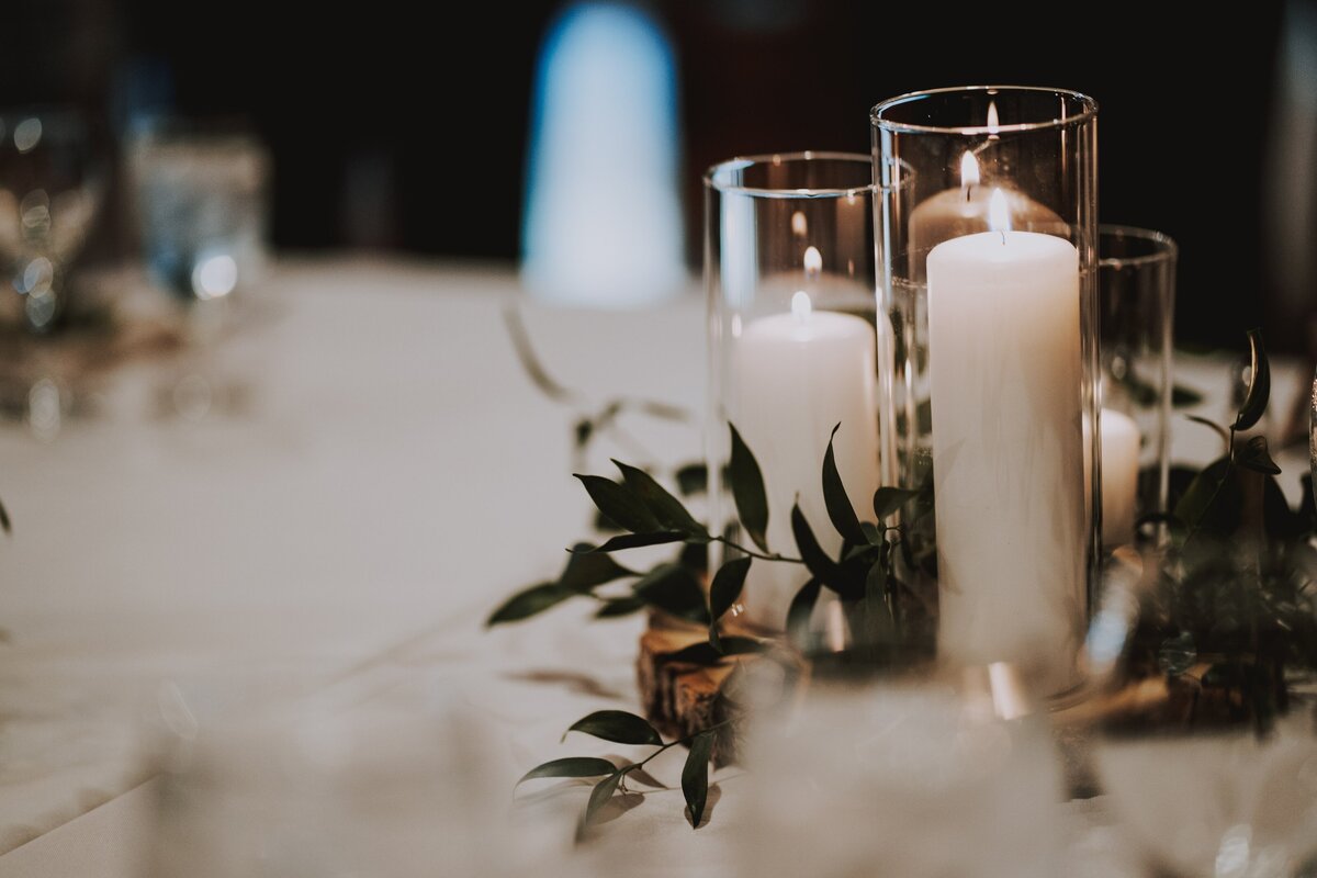 White candle and greenery centerpieces with ivory linens and wood cookies.