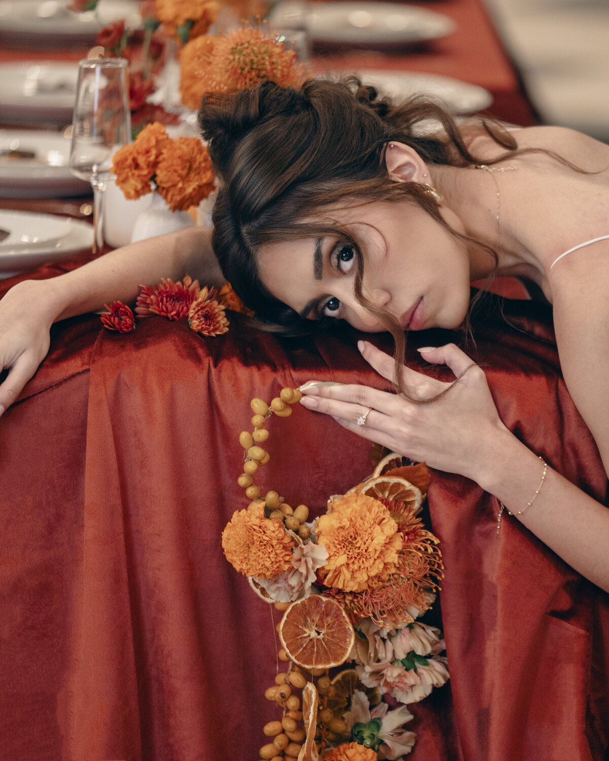 Salt Lake City bridal photographer capturing an artistic portrait of a bride leaning on a rust-colored wedding table adorned with dried floral garland. Moonlit Photo Utah wedding and editorial bridal photography with high-end styling.