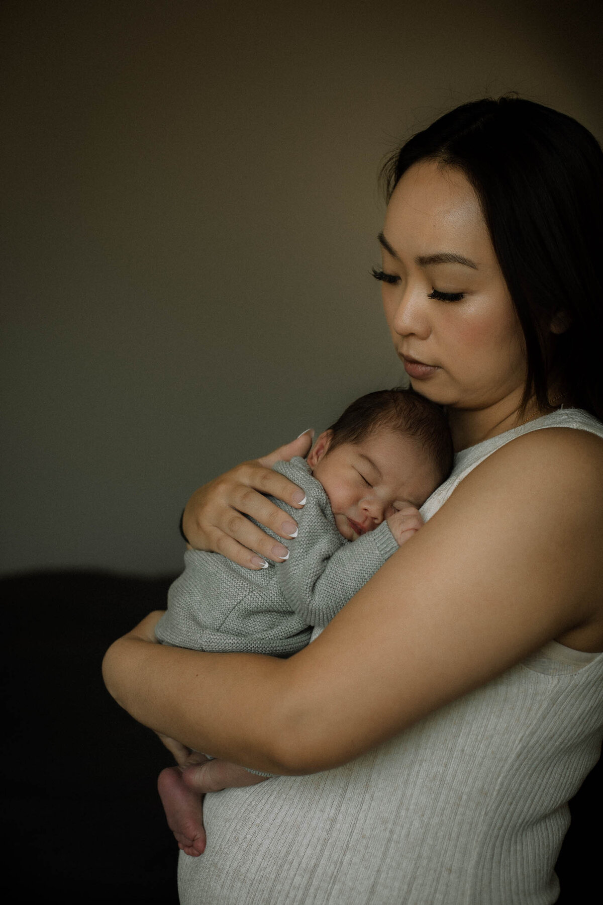 Mom holds her newborn son against her chest while he sleeps and she has a tender expression with her eyes closed.