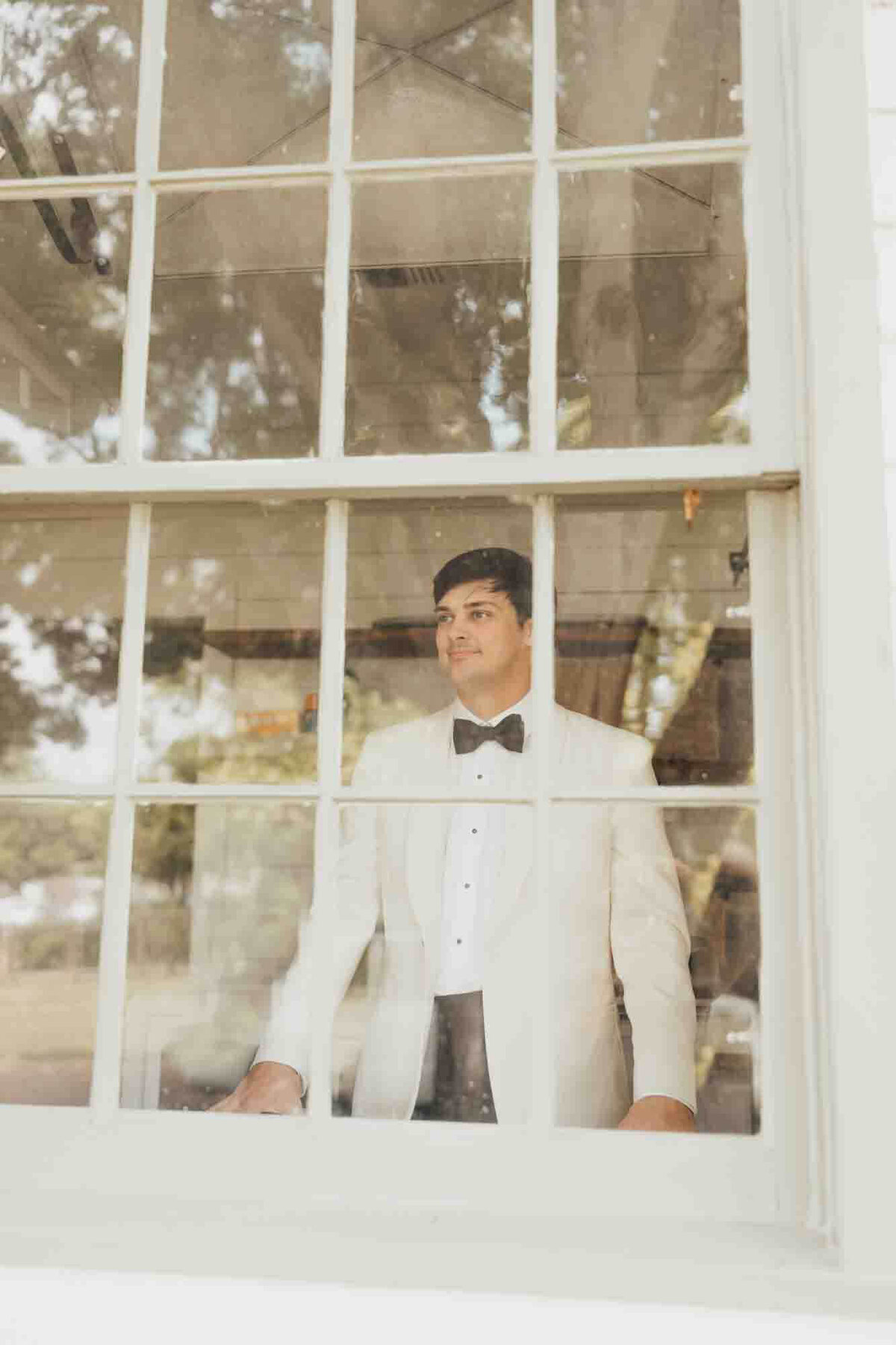 groom looks out of a window on his wedding day, wearing his suit and tie.