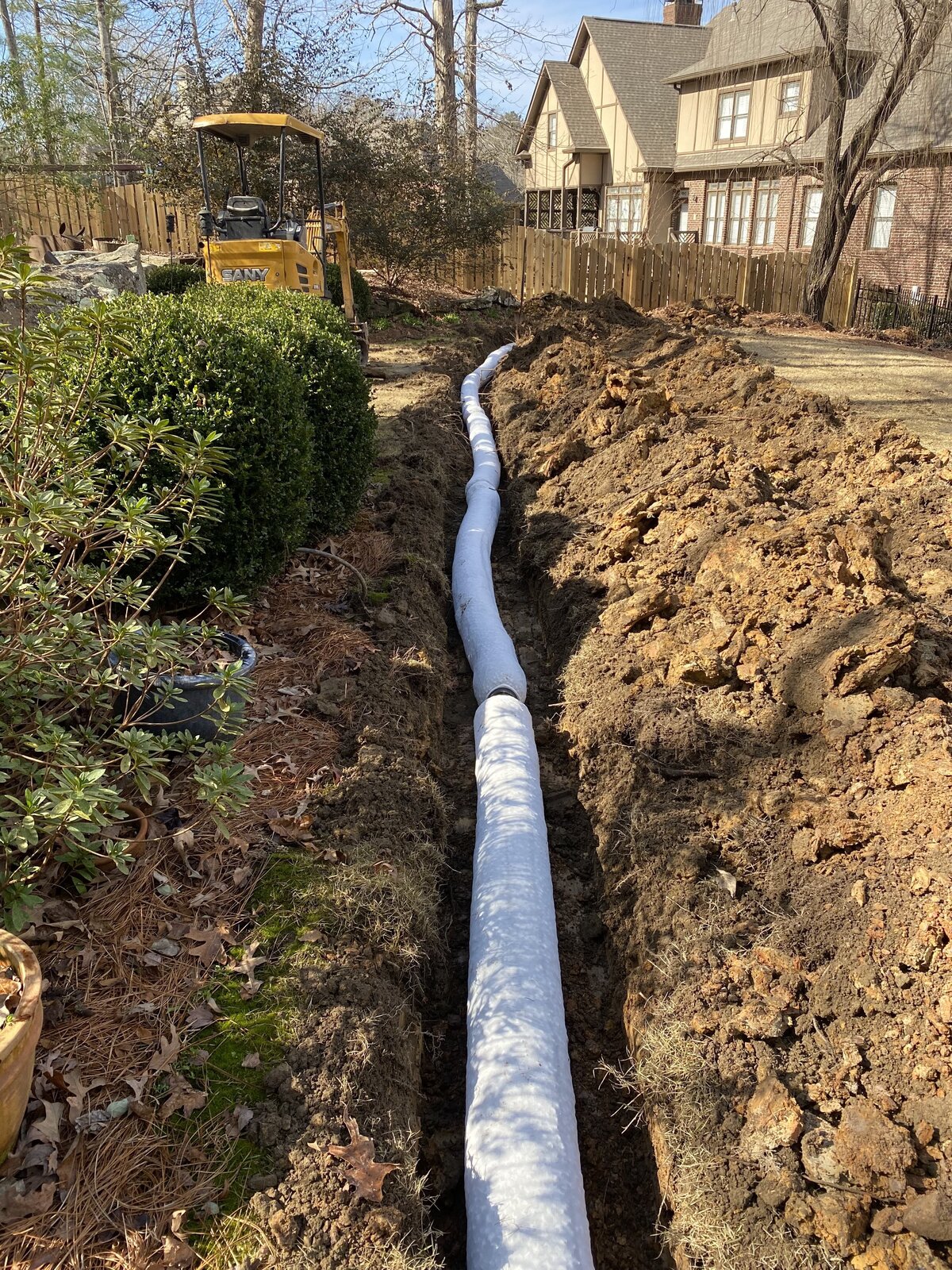 white-pipe-in-dirt-trench-next-to-line-of-green-bushes