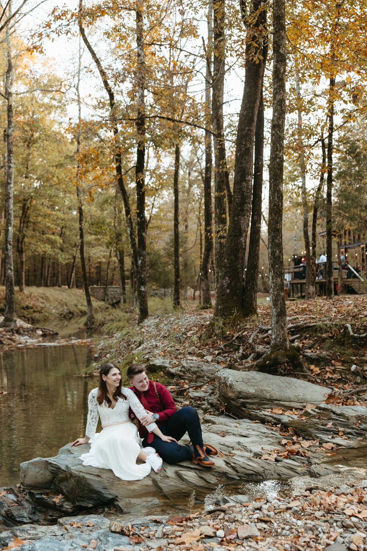 Couple seated on a rock by a creek surrounded by autumn trees