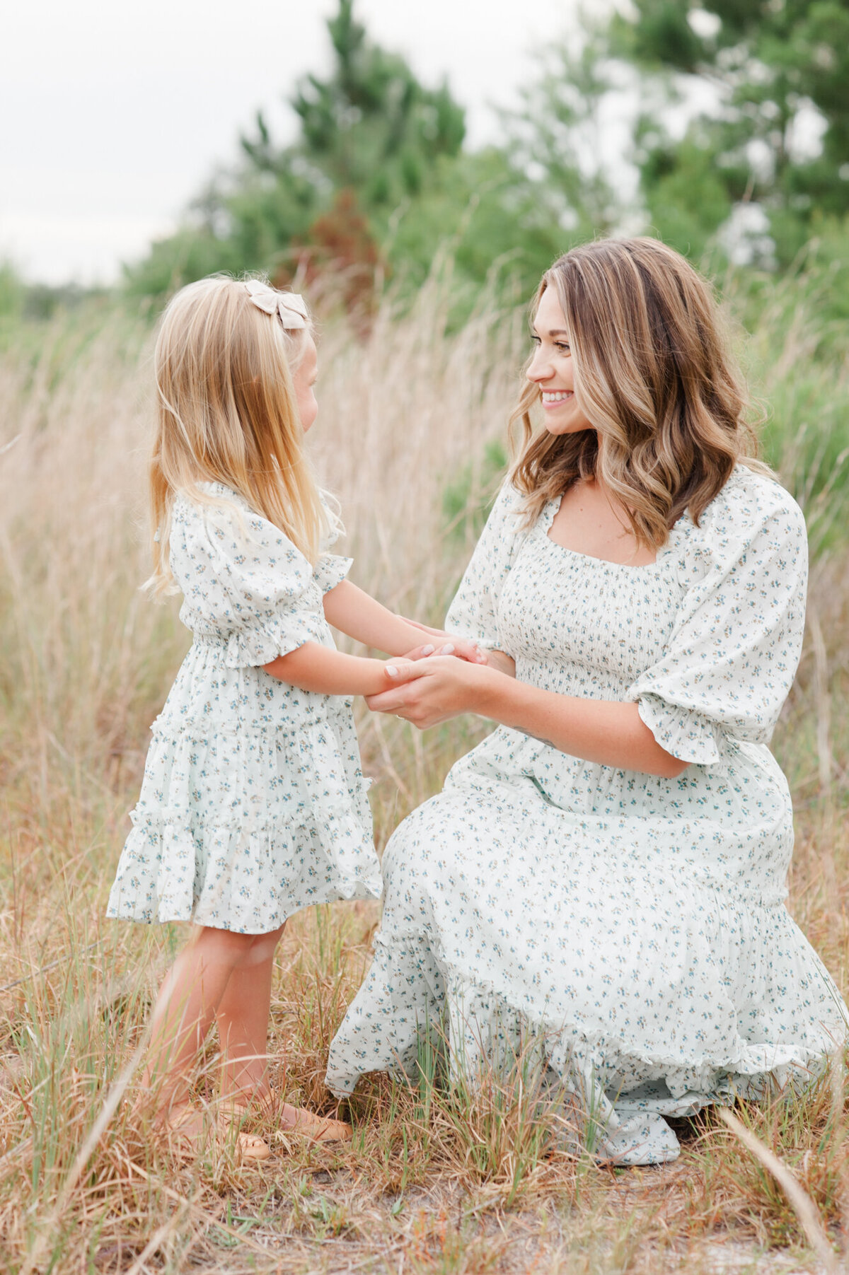 Mom and daughter smiling at each other and holding hands during their family photoshoot