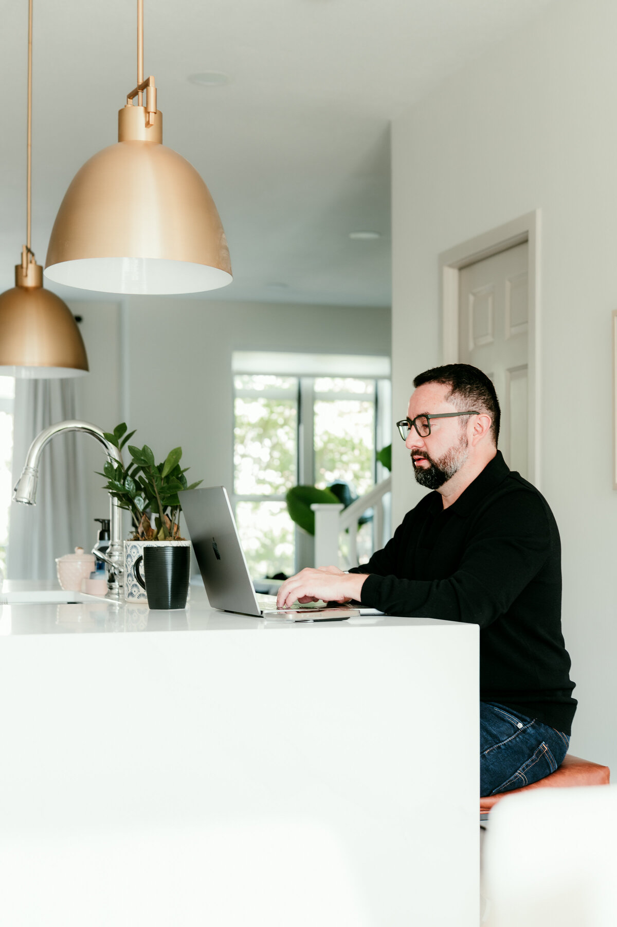 Modern lifestyle dating profile photo of a man sitting at his kitchen island with coffee and laptop in Minneapolis, styled for an authentic dating profile.