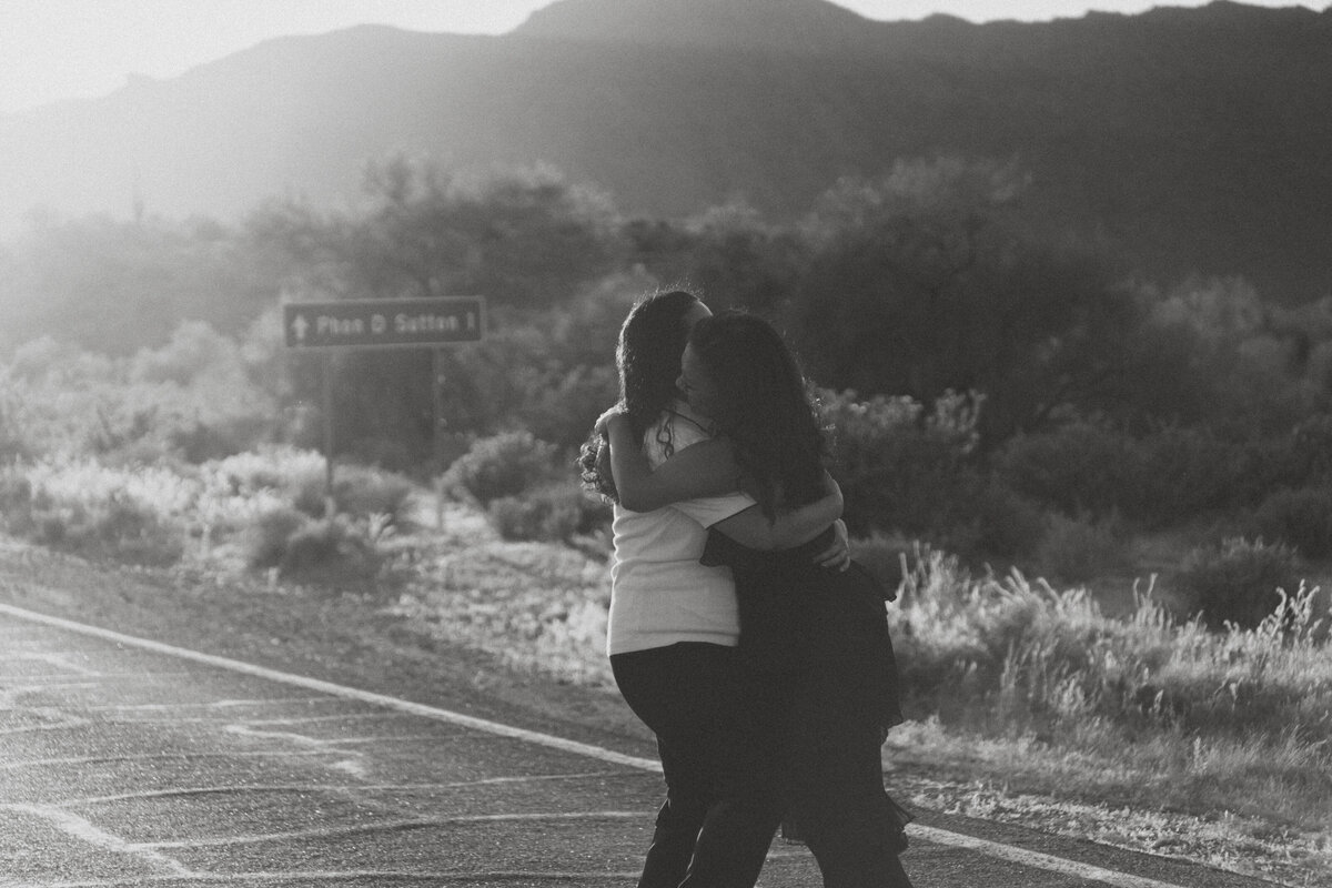 A couple hugging as they stand on a desert road 
