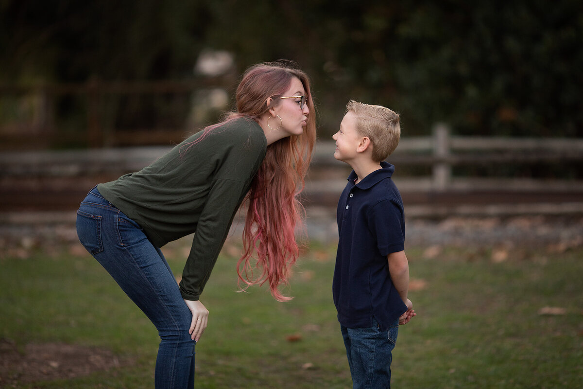 A young girl with pink hair playfully blowing a kiss at her younger brother, smiling together during a family session with a Dallas family photographer.