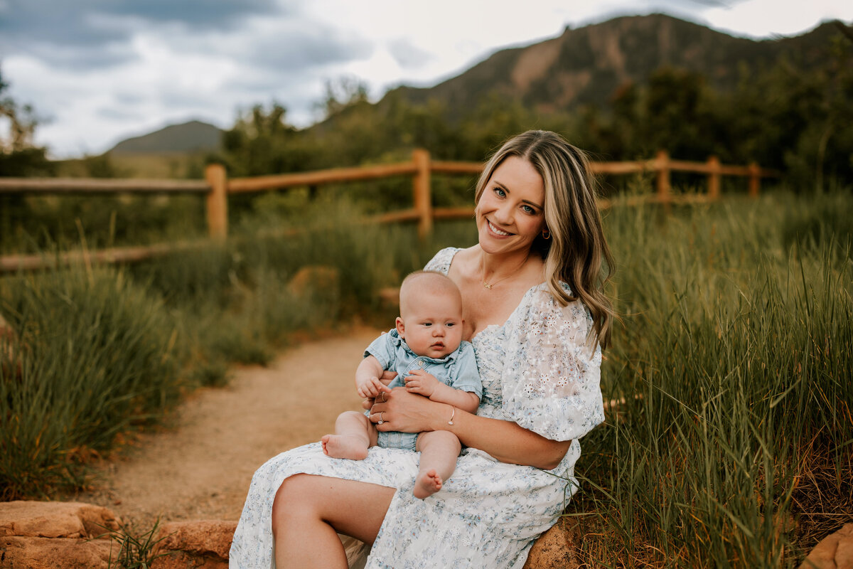 mom snuggles infant son while sitting on large rock steps in boulder colorado