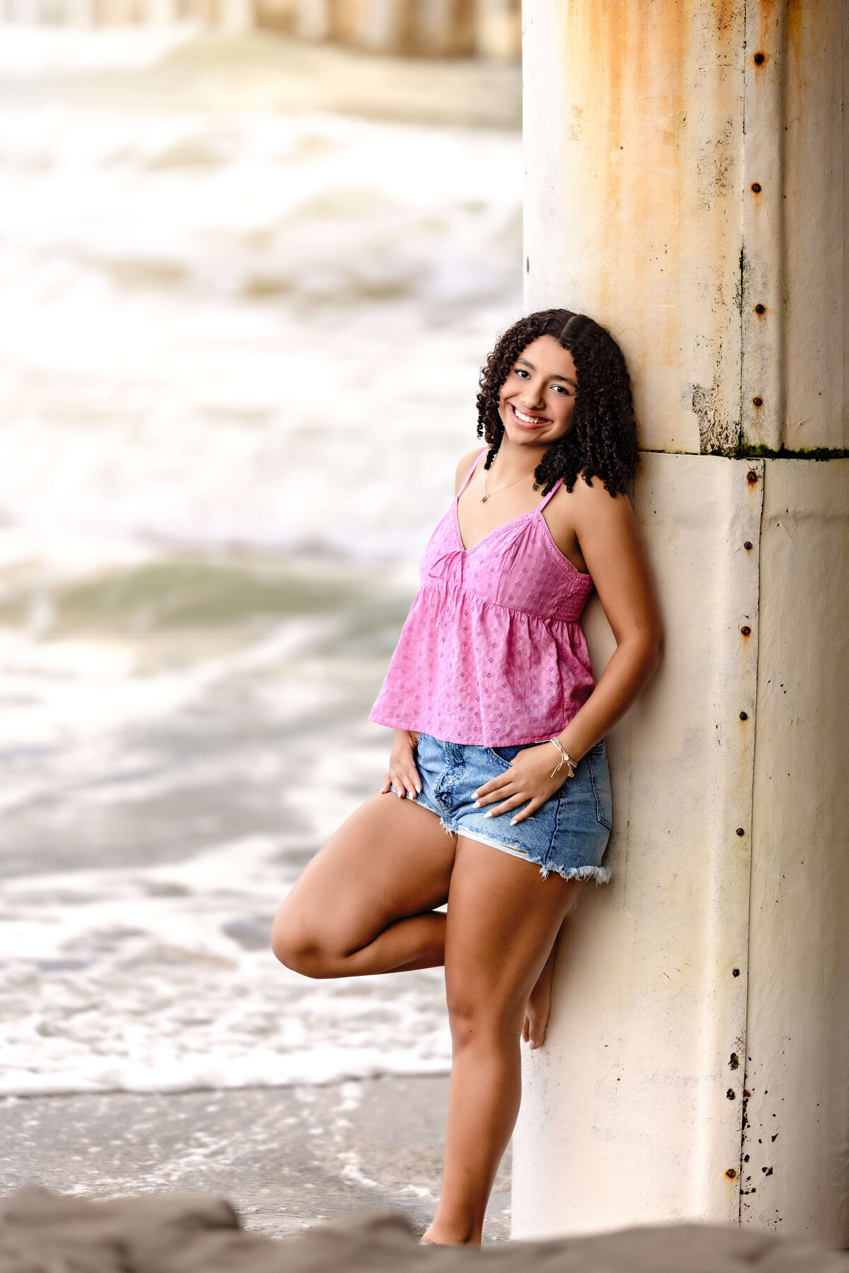 Bold senior photo near the base of Cocoa Beach Pier, girl leaning on concrete pier structure, stormy skies and seas behind her.