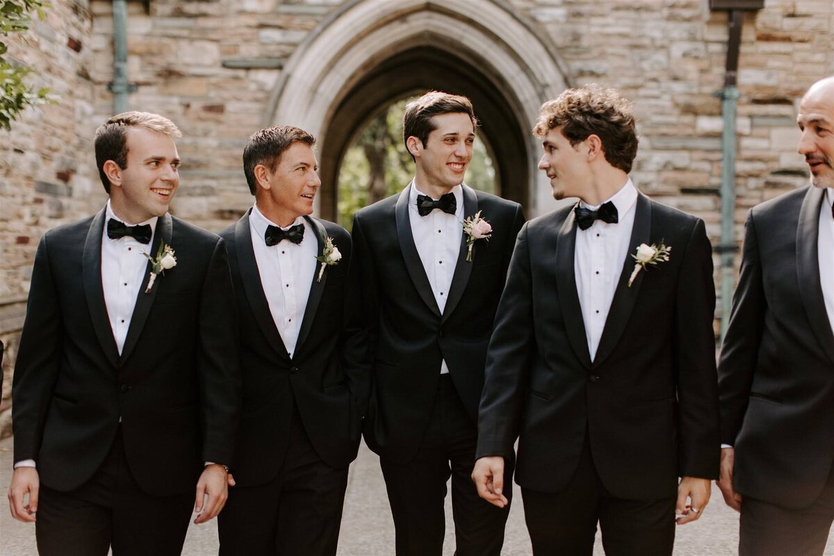 Groom and groomsmen wearing white boutonnieres walking toward camera