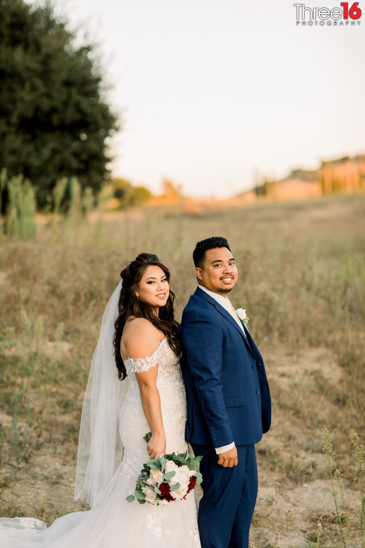 Bride poses for photos behind her Groom in an open field at the Wedgewood Vellano wedding venue