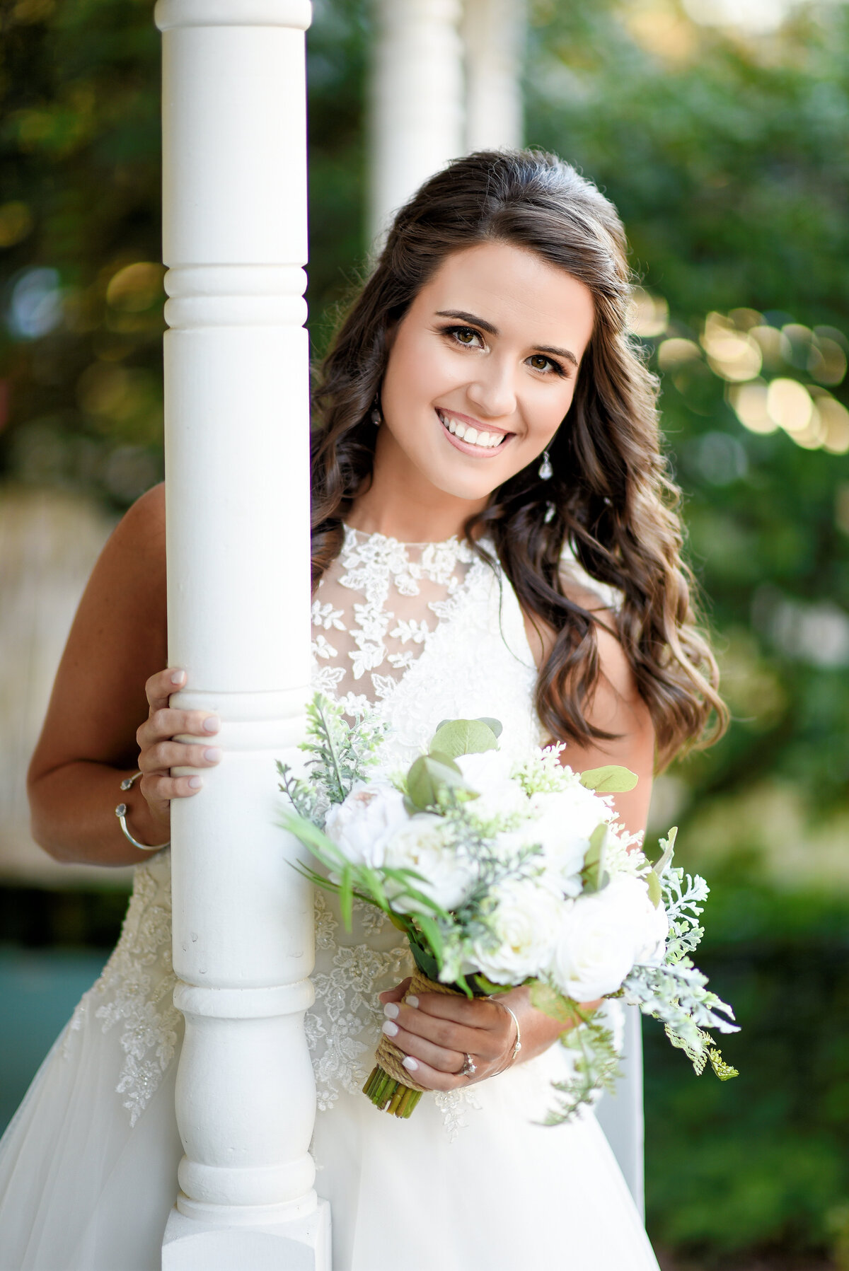 Beautiful bridal portrait photography: Bride leans behind a column from the porch of an old Mississippi farmhouse