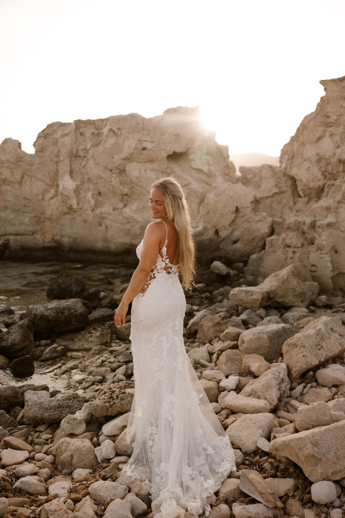 A bride is standing on rocks with her back towards the camera during an after wedding photoshoot on Ibiza