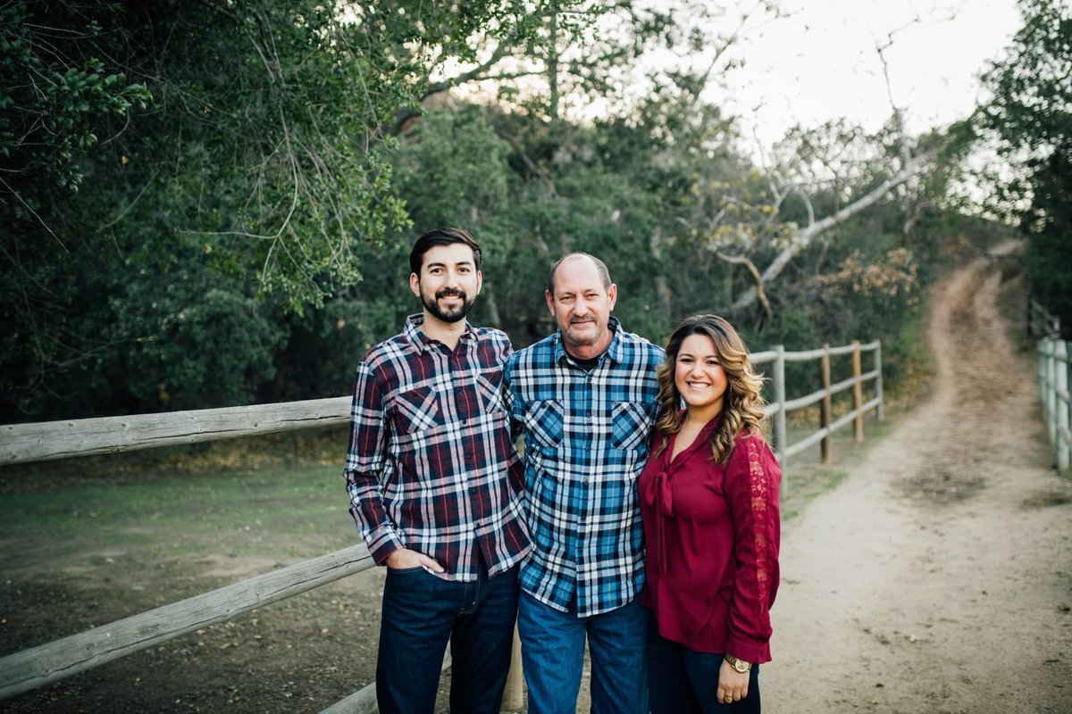 Married couple pose for a family photo with his father along a hiking trail