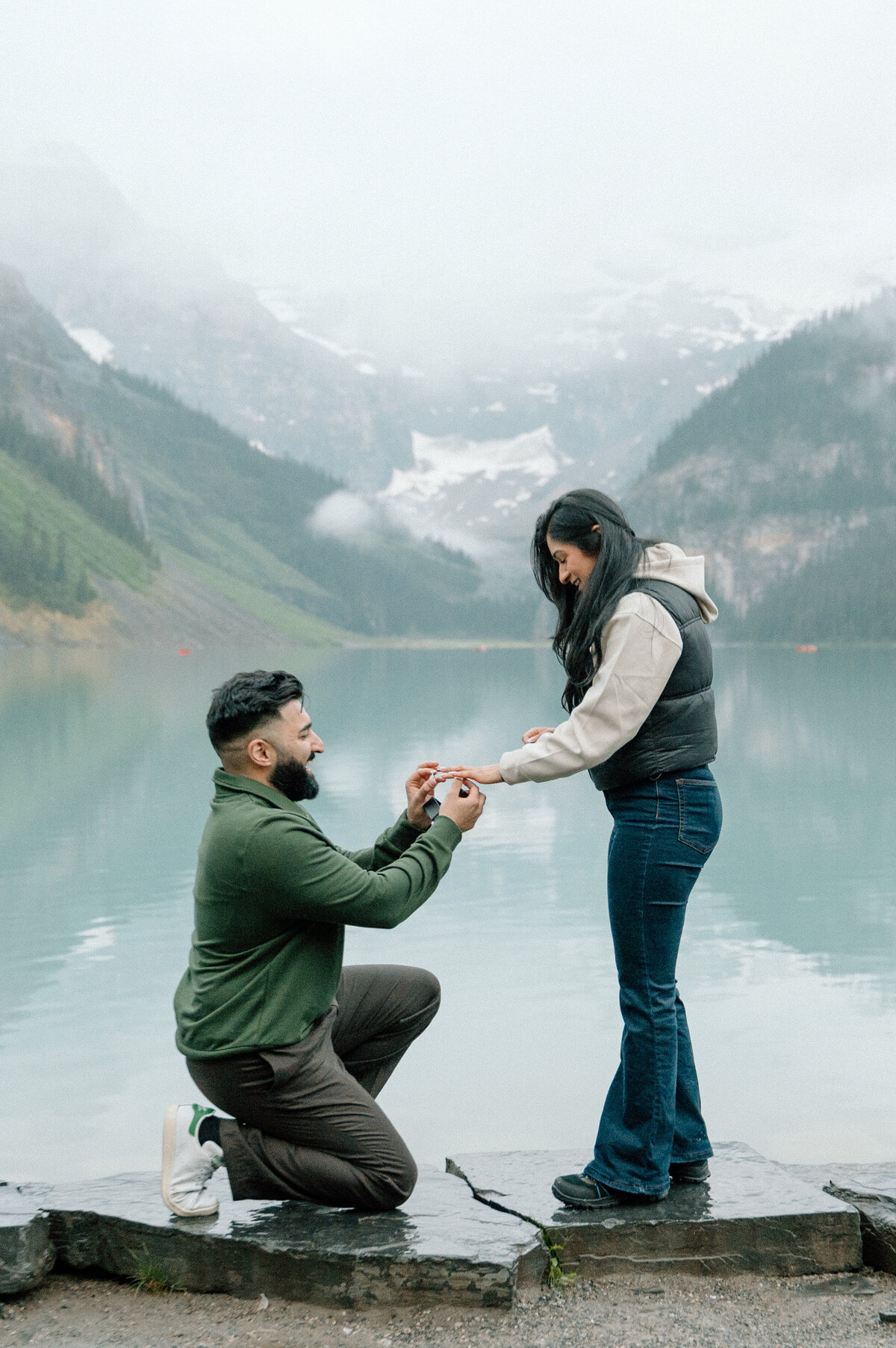 Proposal at Lake Louise with groom-to-be kneeling in front of his fiancee with a turquoise lake and mountains.