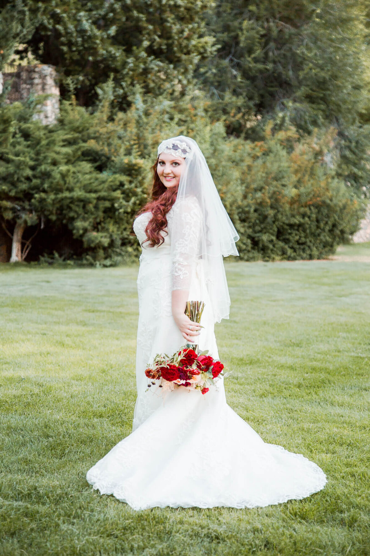 redheaded bride holding a red rose bouquet in a classic bridal pose in a garden field