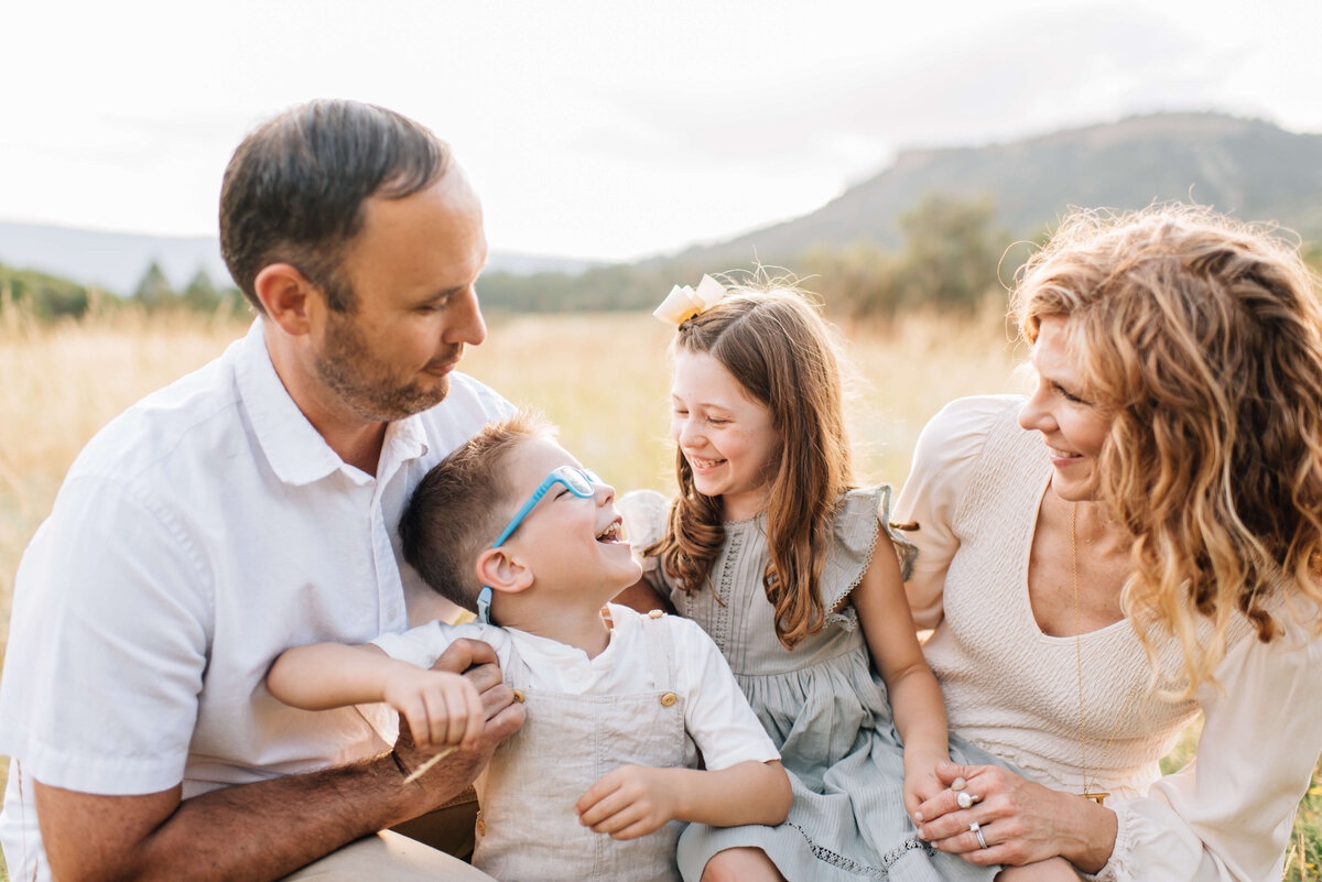 family of four sitting in a field near denver laughing with each other