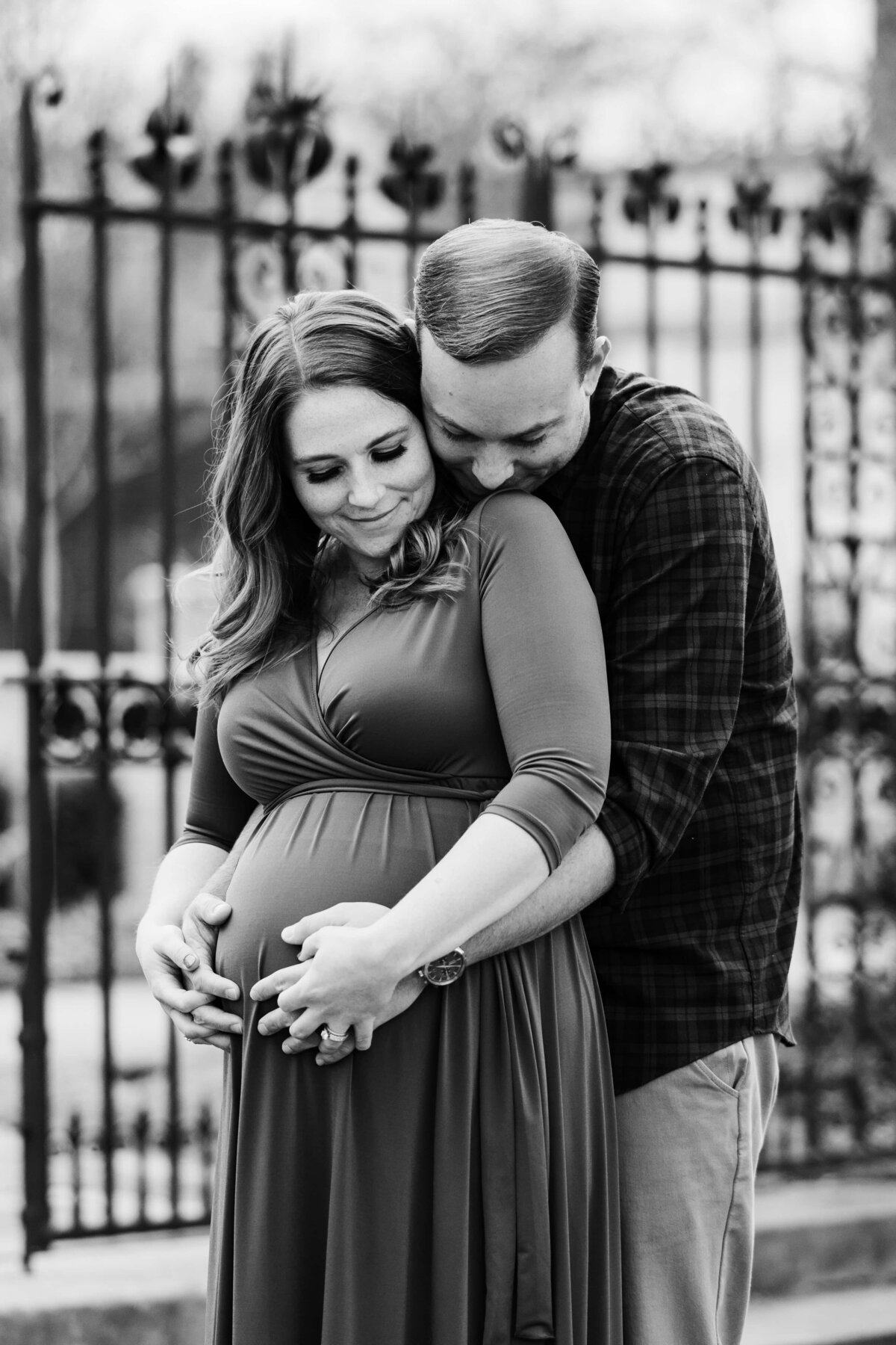 A couple sharing an intimate moment during their maternity photography session, with the man embracing the pregnant woman from behind.