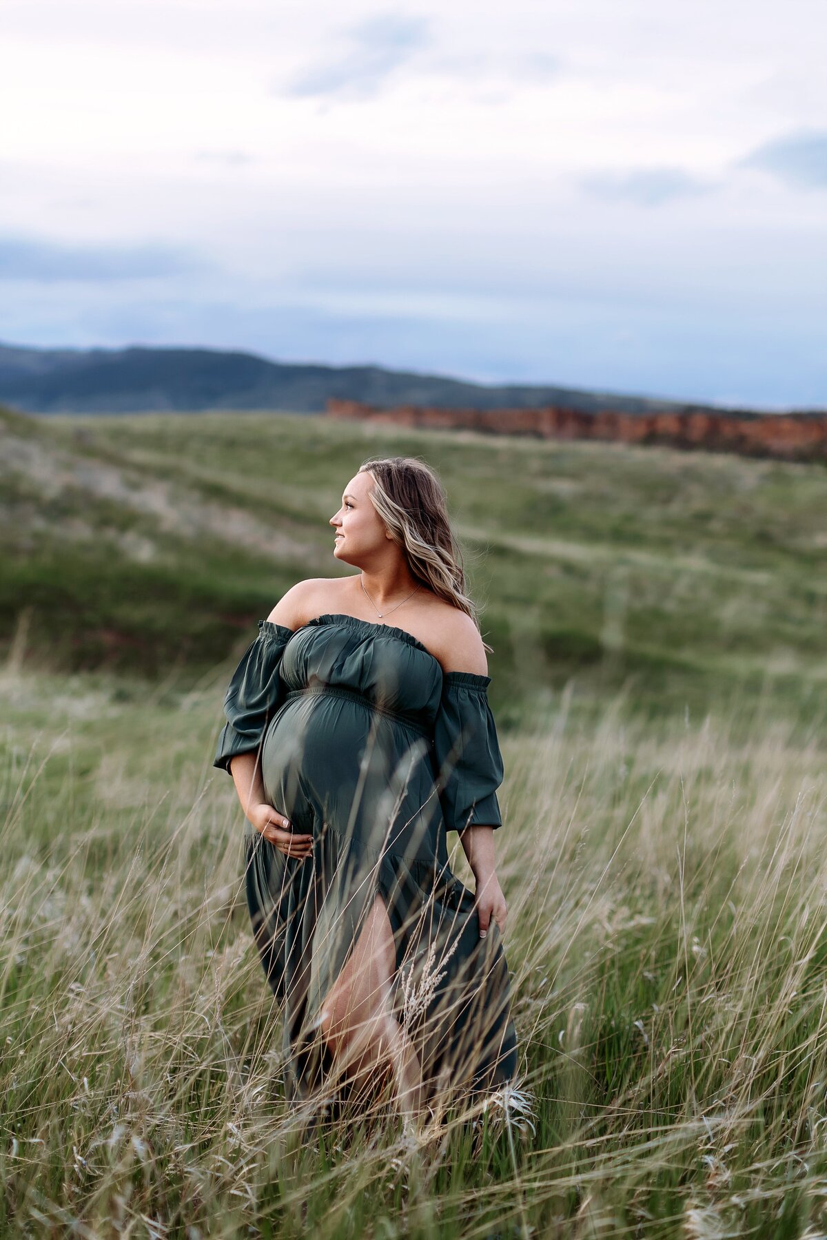 expecting mom standing in the wind at bobcat ridge at sunset holding her bay bump