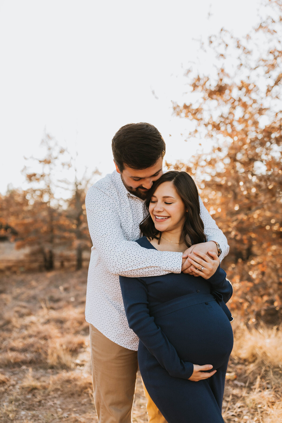 Pregnant couple embracing and giggling together during golden hour