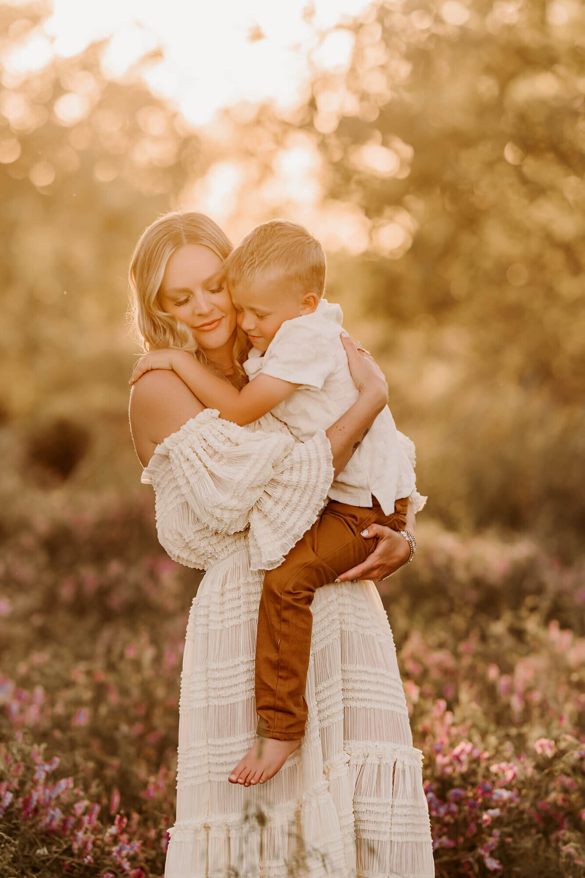 Little boy snuggles his mothers in a field with purple flowers. 