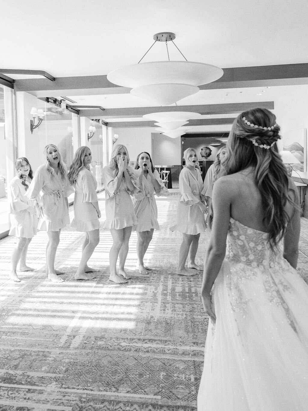 Bridesmaids react with joy and excitement as they see the bride for the first time in her gown. A heartwarming wedding morning moment.