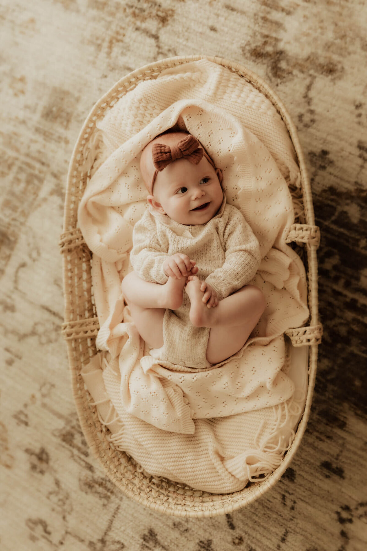 Baby girl laying in a basket while holding her feet.