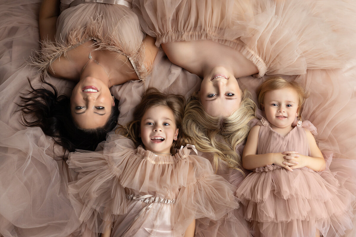 Family of four smiling in matching soft dresses, captured in a Dallas family portrait photography session.