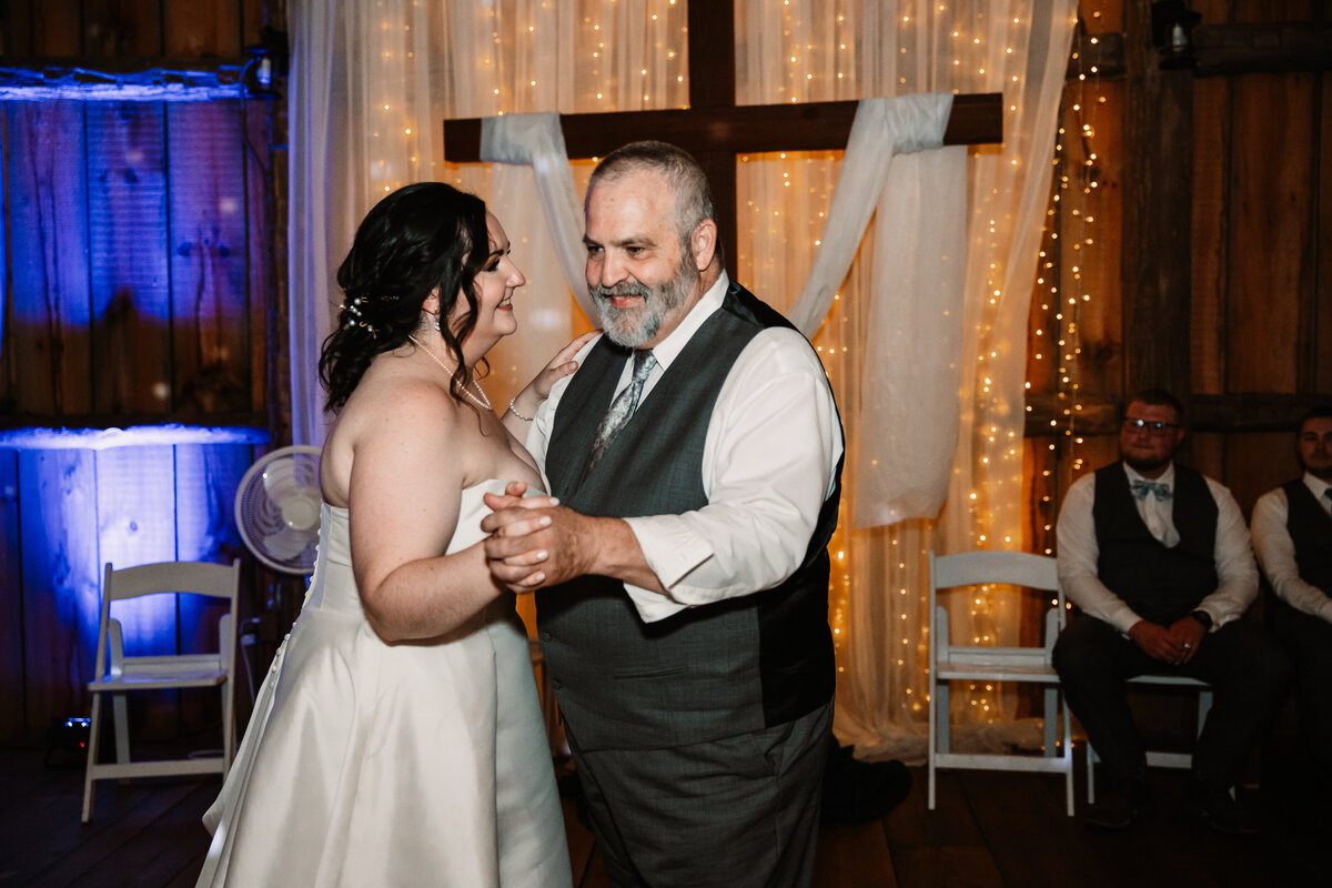 A father in a grey suit dances with his daughter on her wedding day