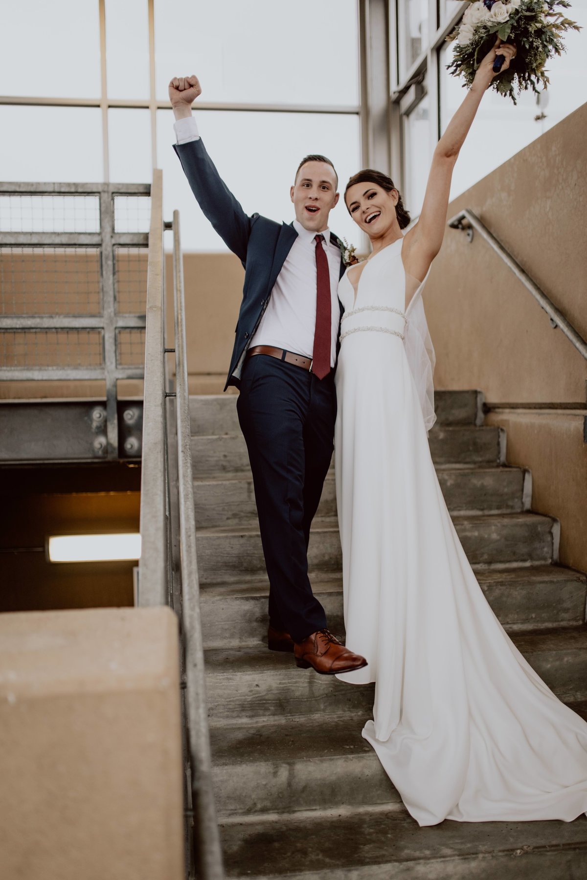 Bride and groom throwing arms up and celebrating their marriage on stairwell.