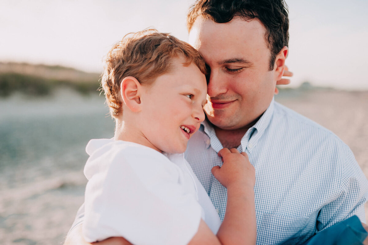 A father holds his young son and snuggles close to his face on the beach