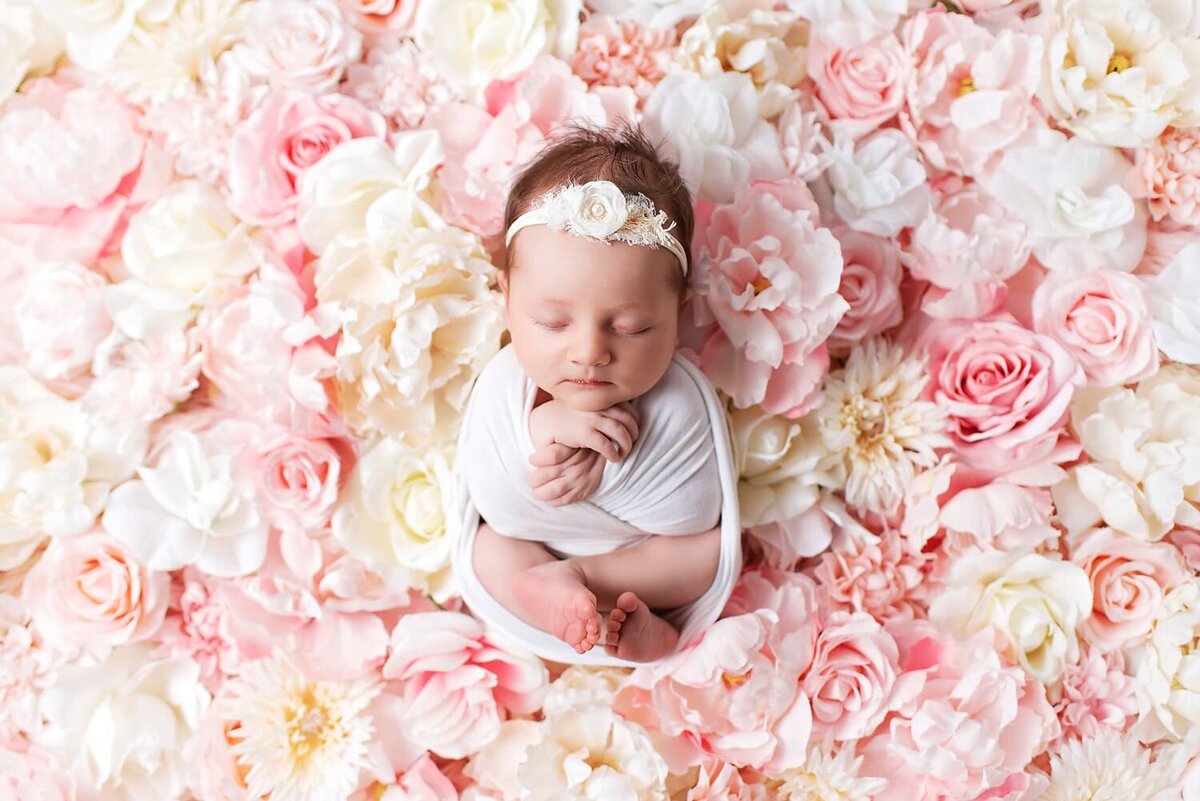 Newborn baby girl in white wrap surrounded by pink flower nest