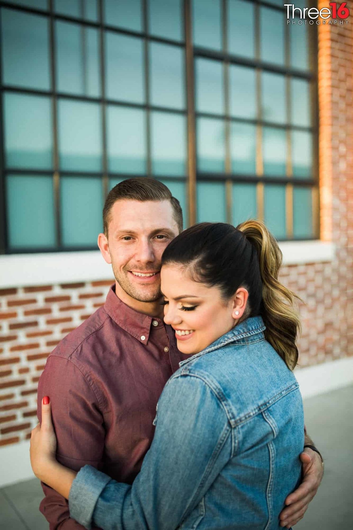 Engaged couple cuddle up as they pose in front of a brick building near the Orange Train Station