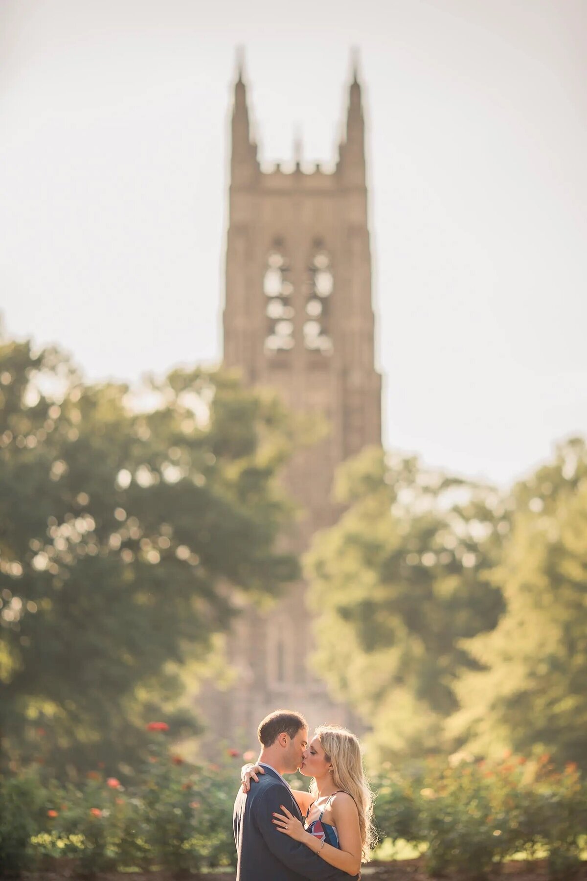 A couple kissing in the foreground with the blurry spire of a gothic cathedral in the background.