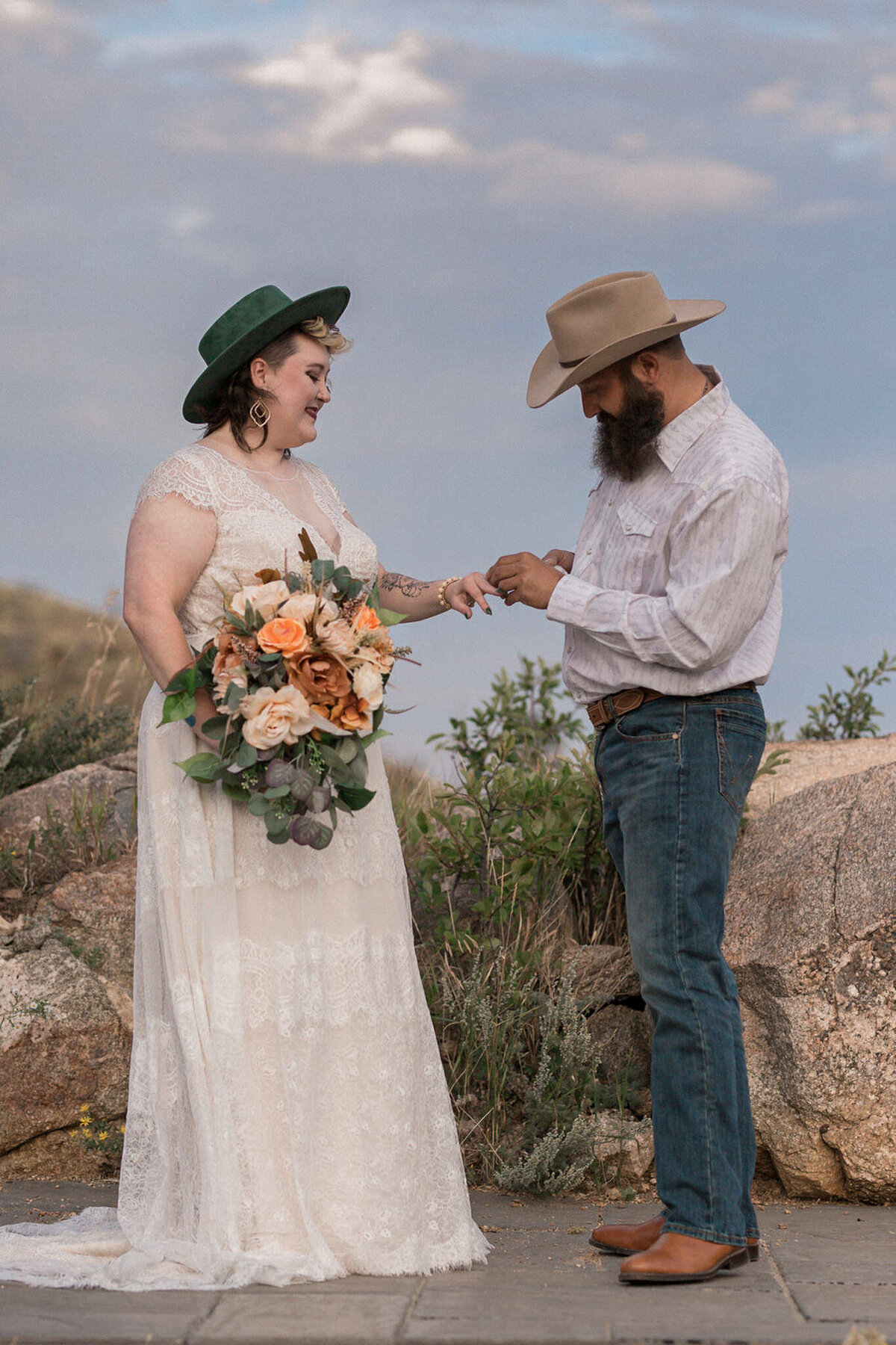The groom , in full cowboy attire, places the ring on his new wife's hand.