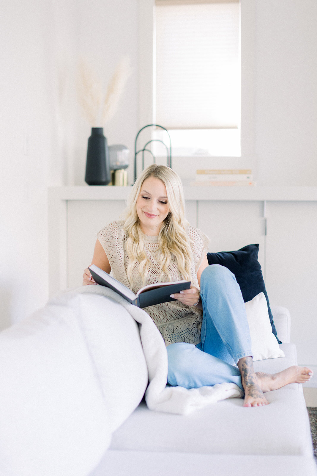 Blonde woman reading on white couch in a bright and airy room