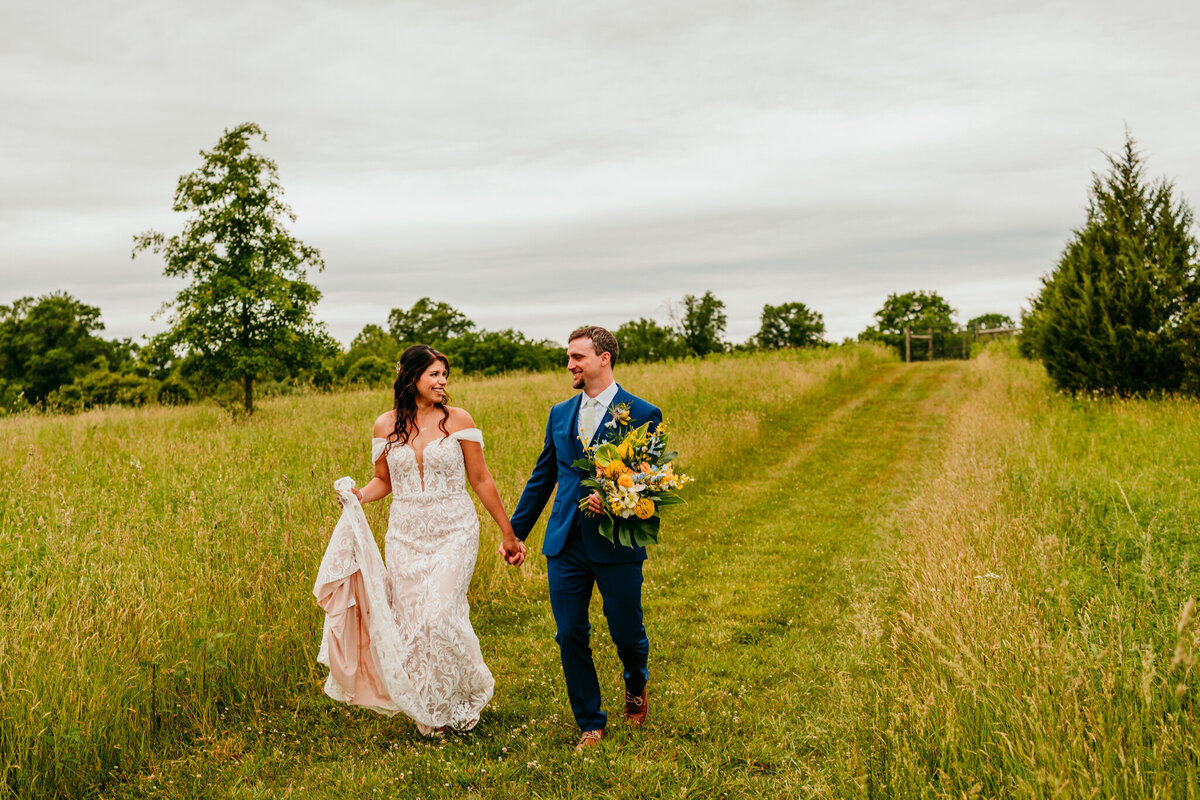  Bride and groom holding hands while walking through a green field during Virginia
elopement