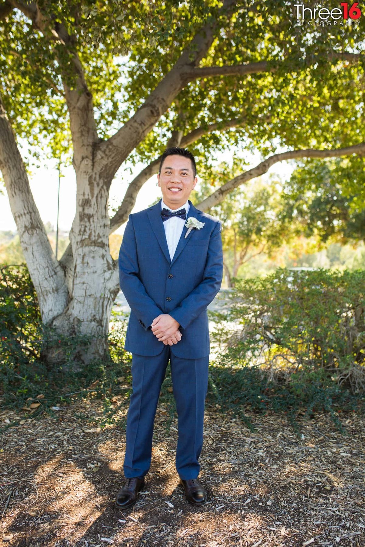 Groom poses in his blue suit under a tree