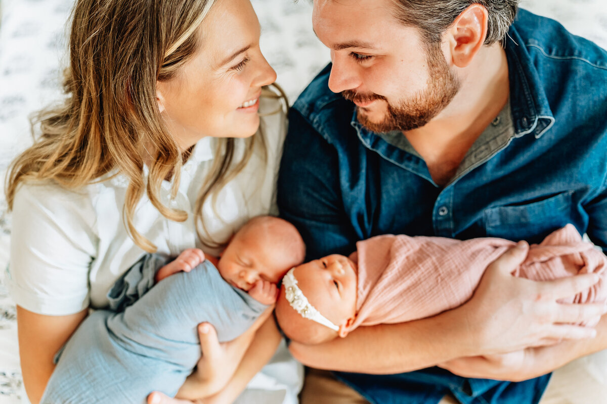 A close-up image of a couple sitting together, each holding one of their newborn twins in their arms.