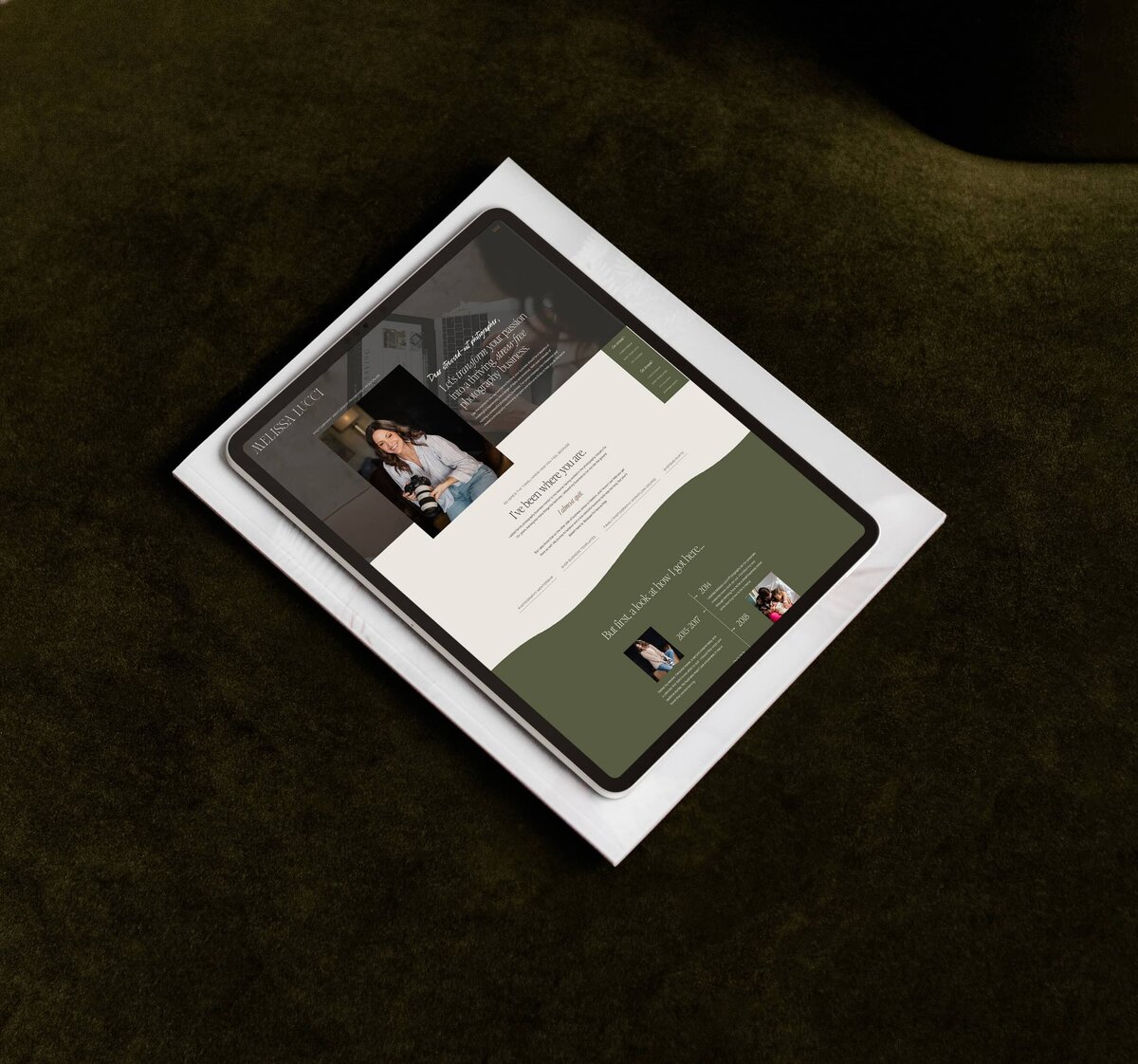 A tablet displaying a photography website with a dark green background and a white text area, showcasing images and text, is placed on a white envelope against a dark green surface.