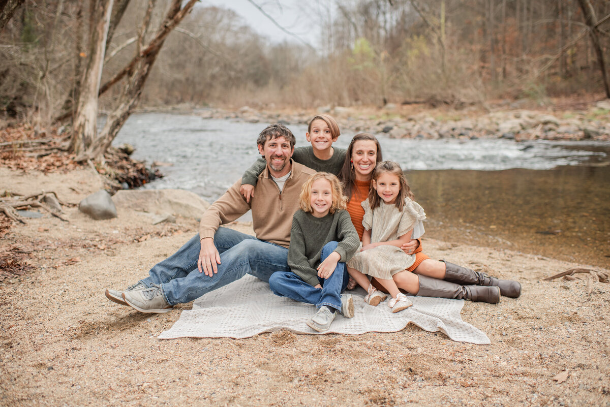 family snuggles on a riverside for a warm winter family session - maryland family photographer