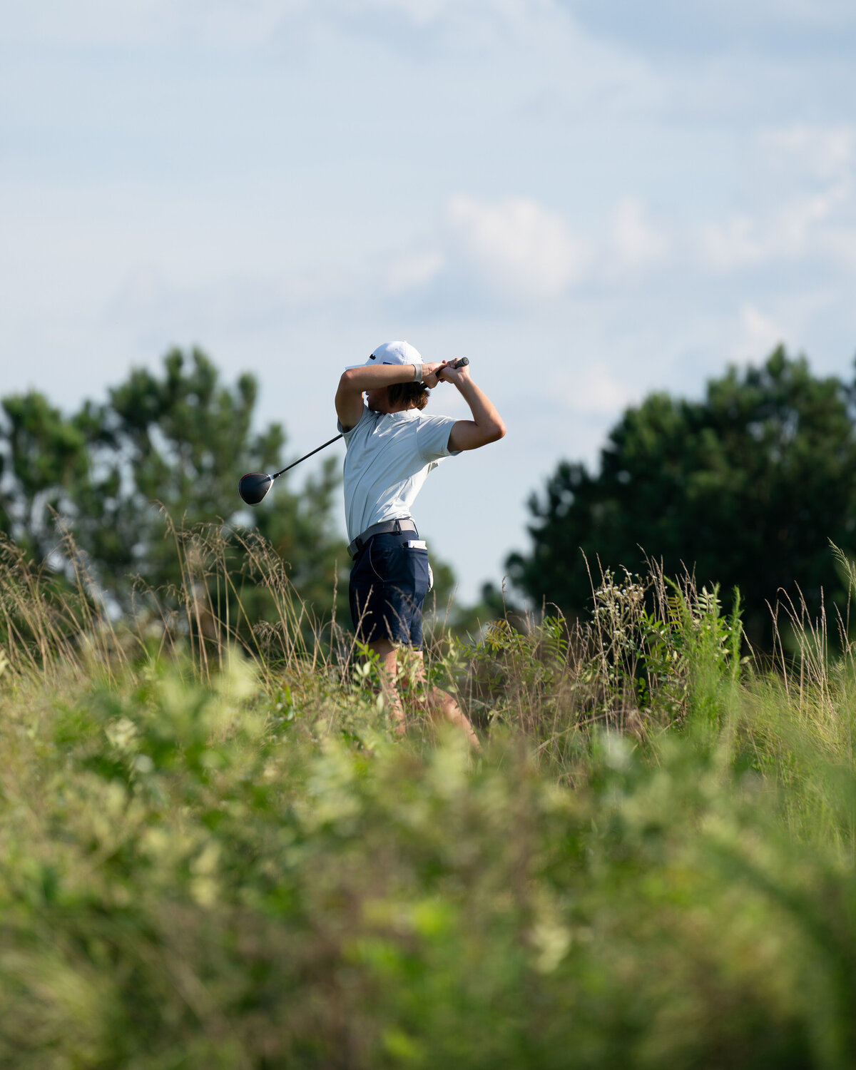 Golfer hitting ball from tee-box at Tobacco Road in Sanford, NC. Photo is taken from a lower angle with wild grass framing bottom of golfer's body.