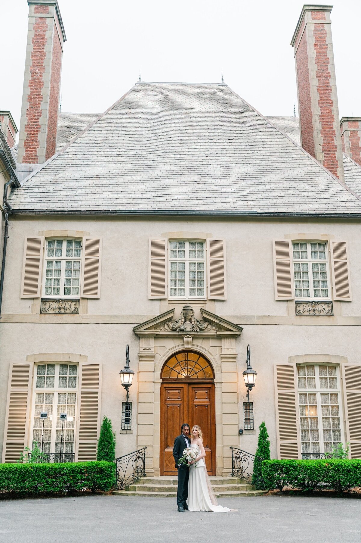 The exterior of Glen Manor House with a bride and groom smiling on the front steps. 