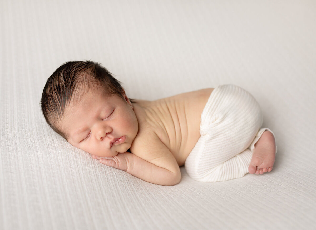 newborn baby boy in white pants posed for newborn photography